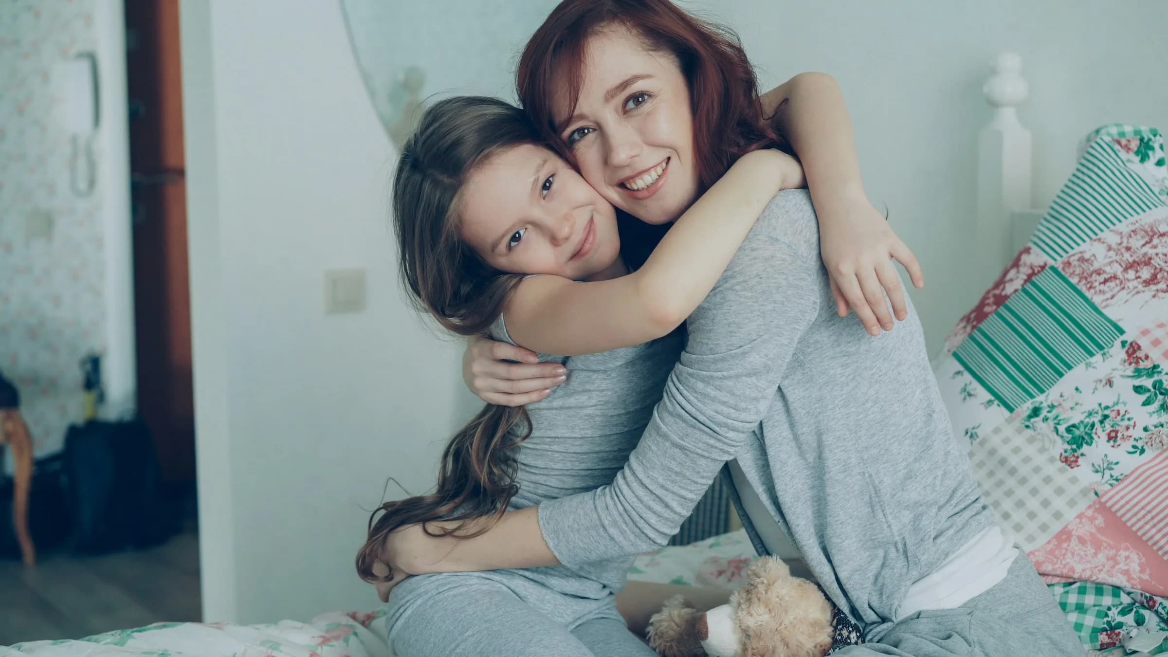 Madre e hija sonriendo abrazadas en su habitación en casa