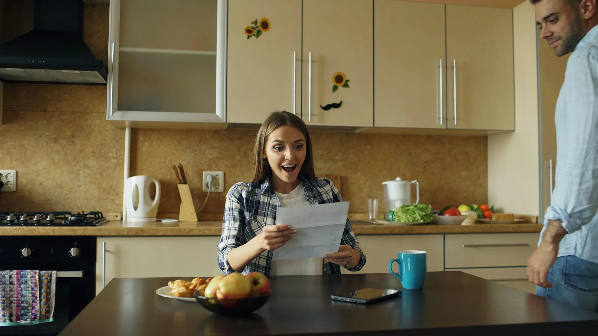Pareja leyendo una carta con buenas noticias en la cocina de su casa