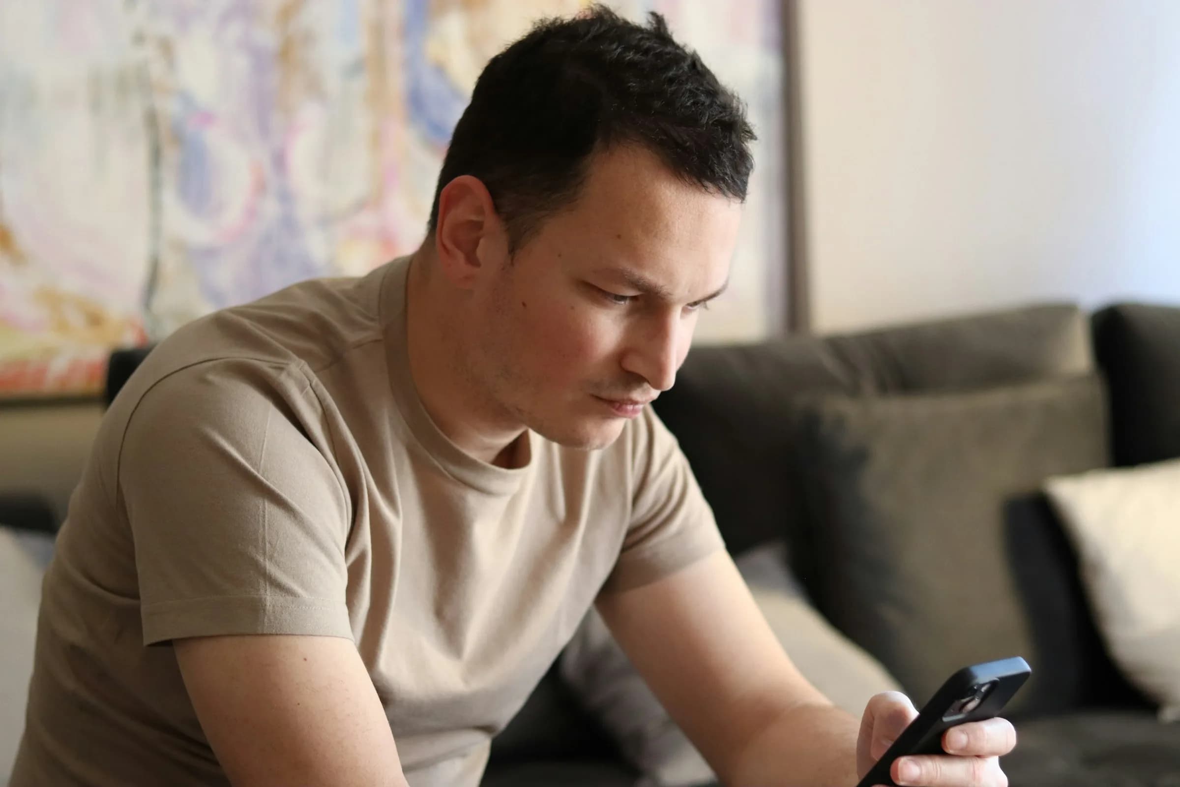 Hombre sentado en el sofá de su casa revisando su crédito en el celular con expresión pensativa